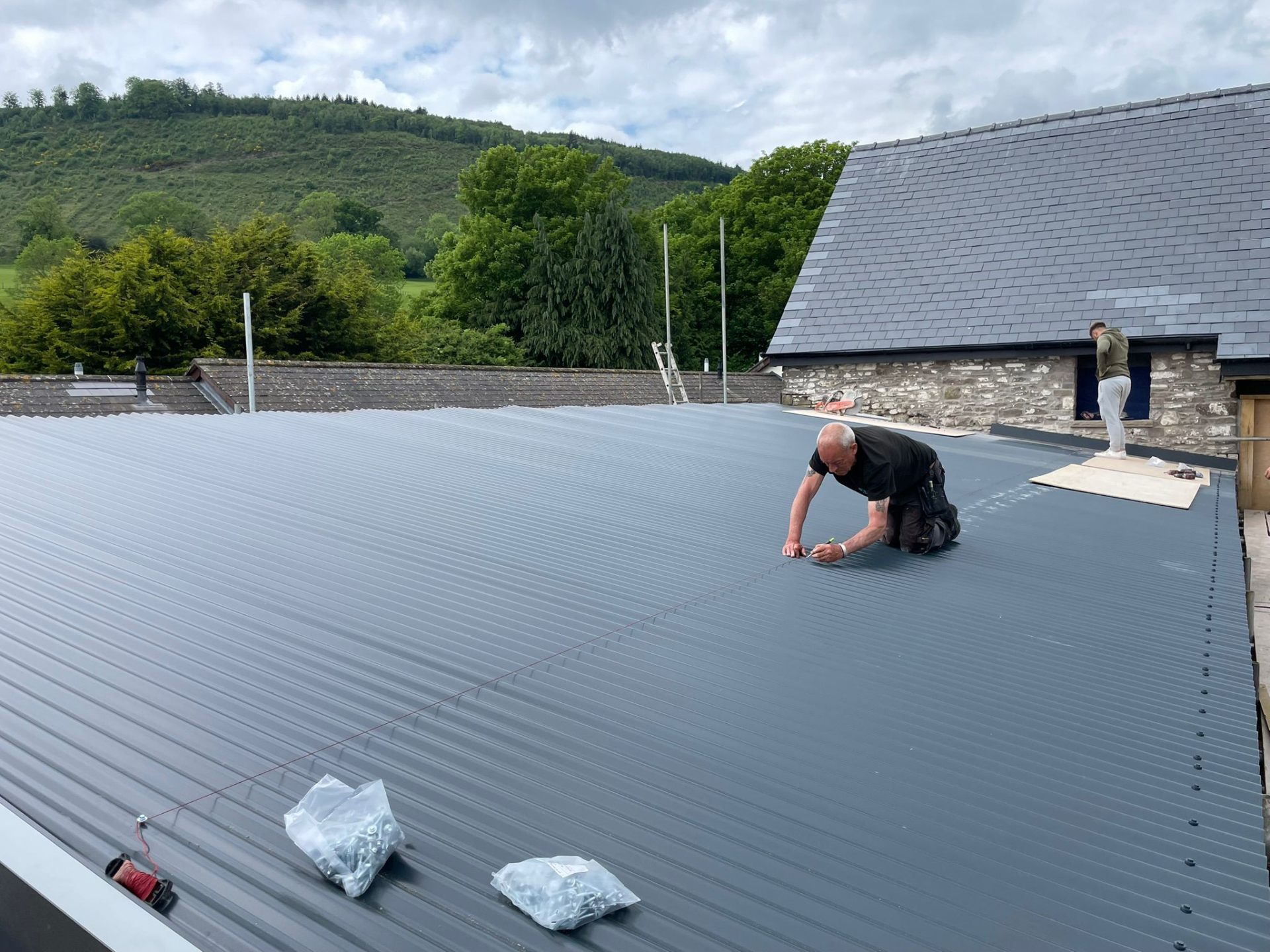 Roofer installing corrugated metal roofing sheets on a commercial building in South Wales
